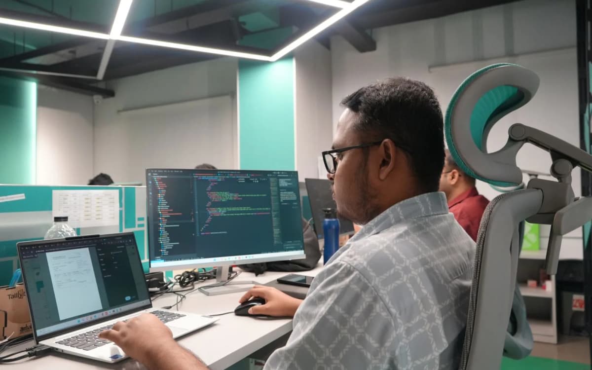 A Girmairi offshore developer reviewing application code on a large monitor in the Dhaka office